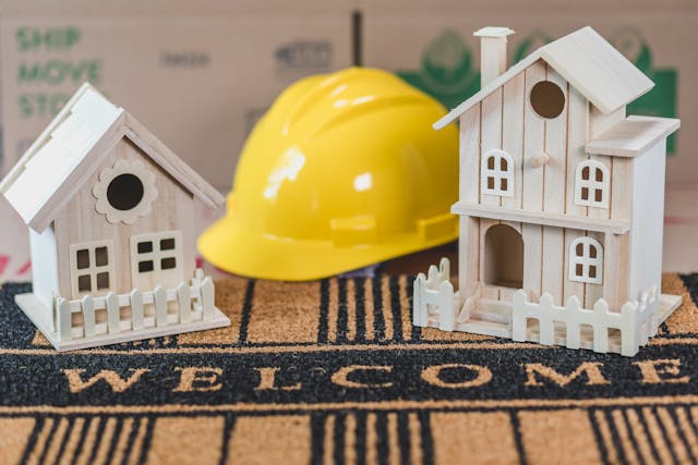 Miniature Houses Beside a Hard Hat on Welcome Sign