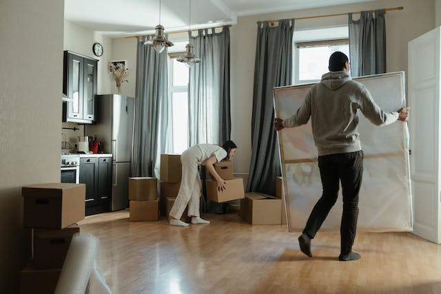 a couple moving into a new home carrying boxes and artwork