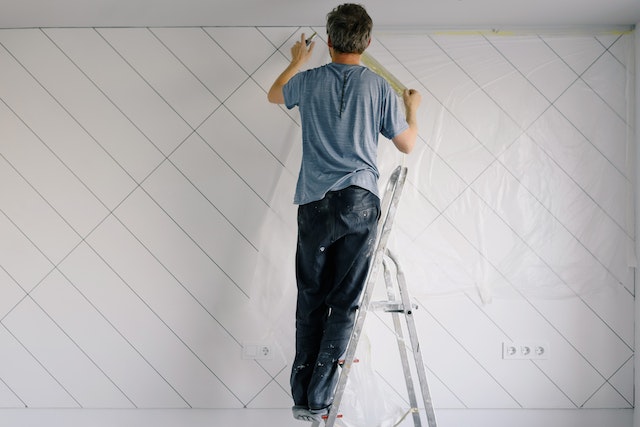 a home painter standing on a ladder touching up a white and grey accent wall
