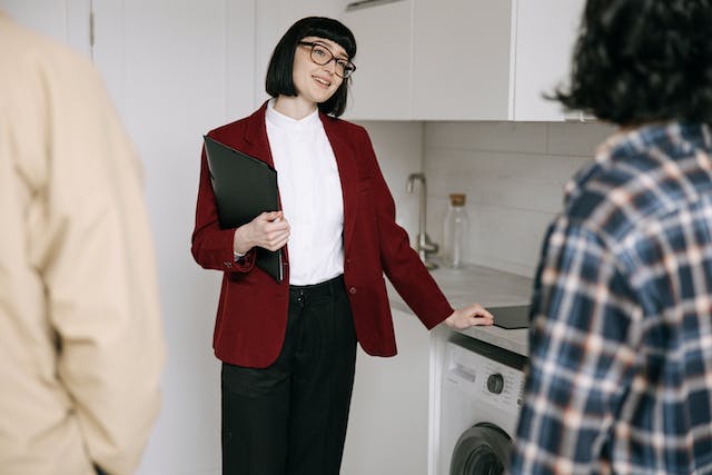 a landlord in a red jacket smiling and holding a lease while talking with two tenants