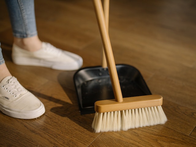 a wooden broom sweeping dirt into a black dustpan