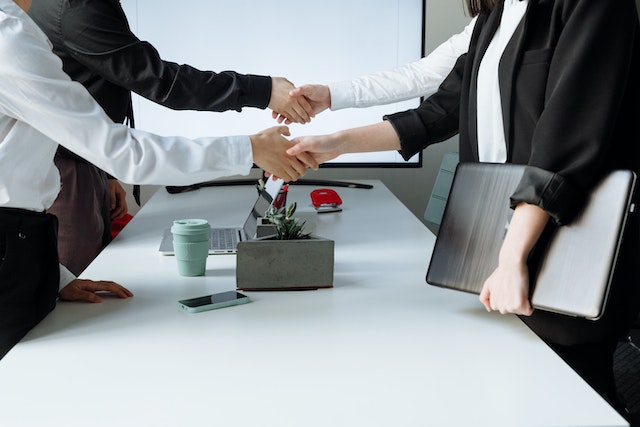 four people standing and shaking hands across a white conference table