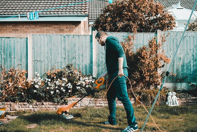 gardener  mowing the grass in front of a flower bed