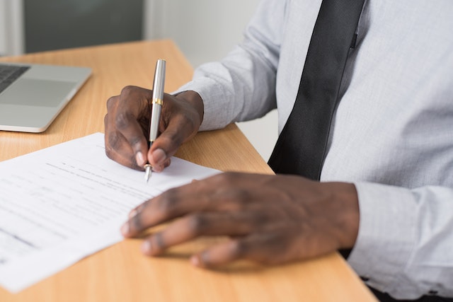 hand holding a silver pen to sign the bottom of a letter