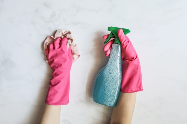 hands in pink gloves holding a spray bottle with a blue liquid in it