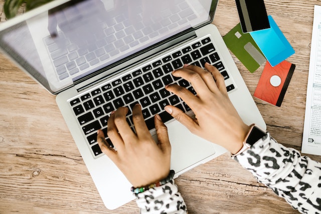 hands typing on a keyboard with a bunch of credit cards on the desk