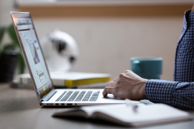 hands typing on a laptop with an open notebook to the computer