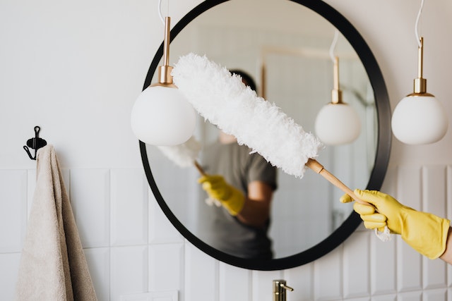 person holding a feather duster to clean a round mirror