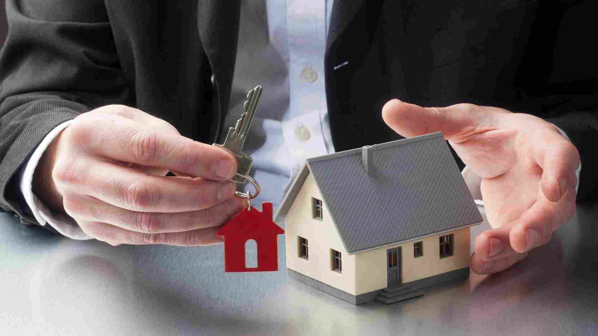 person holding a keychain with a red house on it next to a house figurine