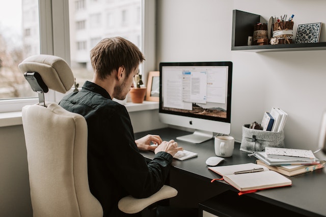 person working at their black desk covered in books and notepads typing up an email