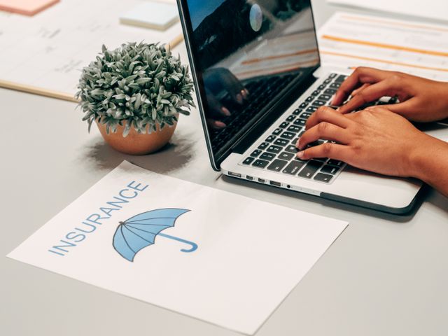 Hands typing on a laptop at a desk with an insurance paper