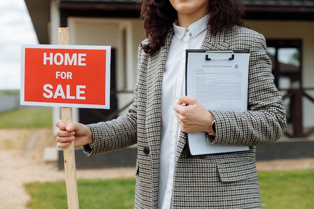 real estate agent holding a home for sale sign and purchasing agreement