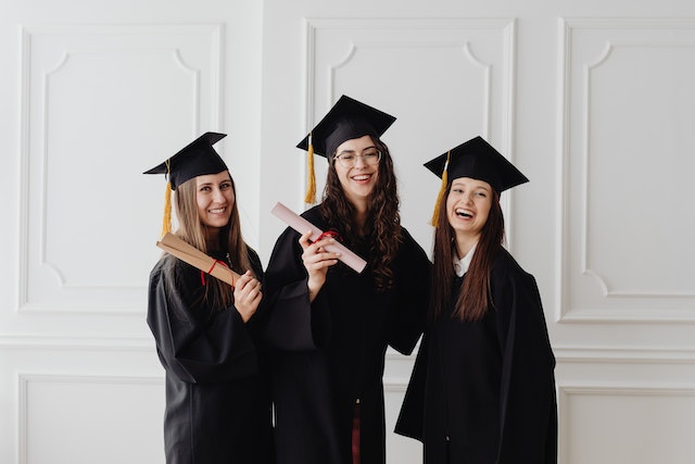three college graduates in their cap and gown with diplomas