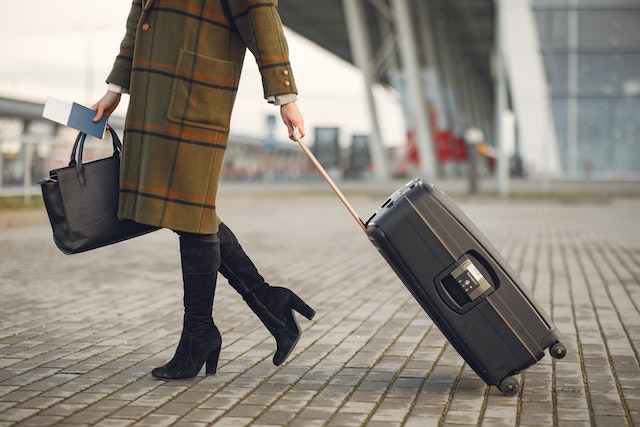 traveler in a long coat pulling a suitcase behind them